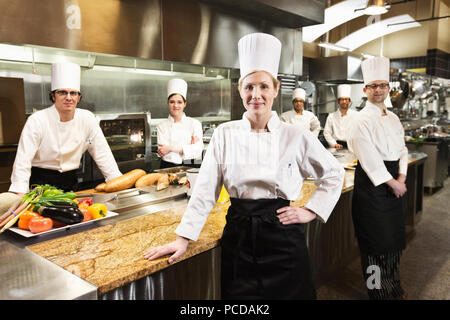 A portrait of a caucasian female chef and her team of chefs in the backgroiund. Stock Photo