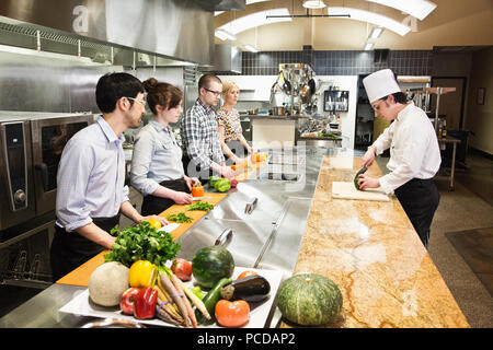 A caucaisan male chef teaching a cooking class for a mixed race grop of students in a commercial kitchen, Stock Photo