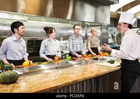 A caucaisan male chef teaching a cooking class for a mixed race grop of students in a commercial kitchen, Stock Photo