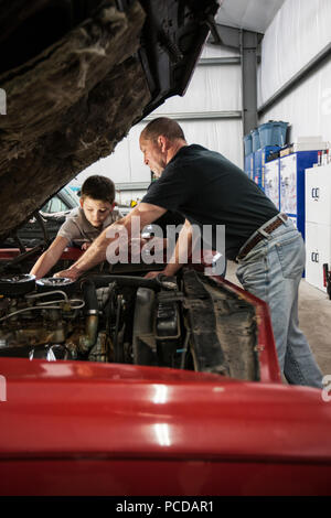 A senior caucasian male car mechanic showing his grandson how to work on a car engine. Stock Photo