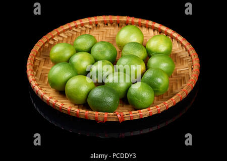Sixteen green limes on wicker plate isolated on black reflecting background Stock Photo