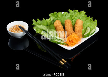 Vietnamese dish Nem ran crispy rolls with vegetables on rectangular white plate isolated on black reflective background. Served with chopsticks and sa Stock Photo
