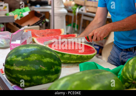 Fruit seller cutting and slicing water melon and putting for sale on a French market stall in Toulon southern France Stock Photo