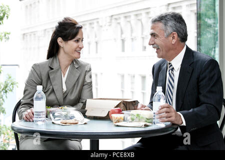 A caucasian businesswoman and a middle eastern businessman having a business lunch in front of  a convention center lobby window. Stock Photo