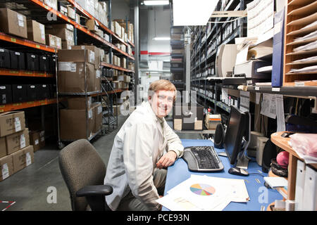A portrait of a caucaisan male technician sitting at his desk in a parts department in a technical research and development site. Stock Photo
