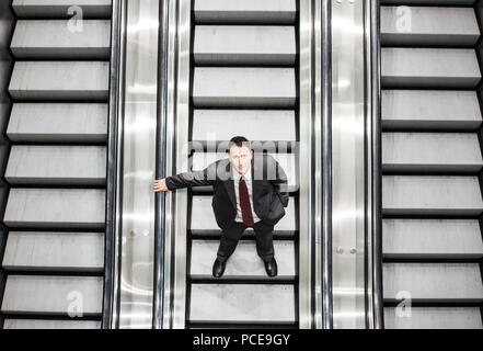Looking down on a caucasian businessman looking up while riding an escalator in a convention center. Stock Photo