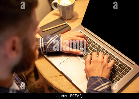 Young man drinking coffee in cafe and using laptop. Man's hands using laptop during coffee break Stock Photo