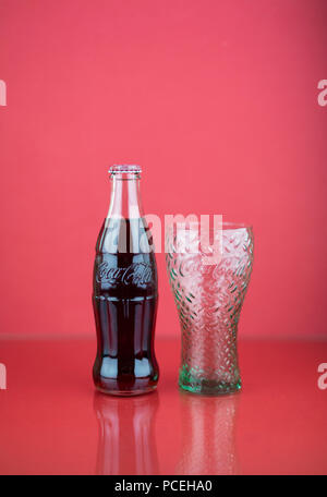 coca-cola contour bottle with embossed logo from Italy on red background with glass and reflection Stock Photo