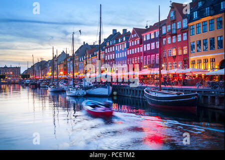 Evening scene with boats moored by illuminated Nyhavn harbor embankment, Copenhagen, Denmark Stock Photo