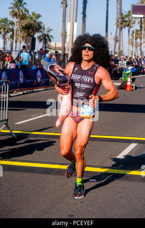 A marathon runner in Hunting Beach, CA, crosses the finish line wearing a fright wig and an inflated female figure, explaining cryptically that 'It's about the beach.'  (Photo by Spencer Grant) Stock Photo