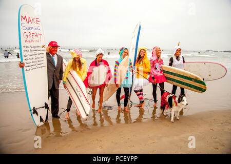 Wearing fanciful costumes including a rabbit and a unicorn and hefting their surfboards, six women and a dog in a skirt line up at a Halloween costumed surfing event in Huntington Beach, CA, as they are joined by a man dressed as Donald Trump.  (Photo by Spencer Grant) Stock Photo