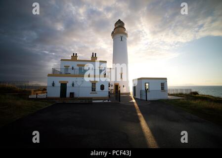 The sun shining brightly behind Turnberry Lighthouse at the Ayrshire Coast next to the Trump Turnberry Golf Course, at sunset, with a clear blue sky. Stock Photo
