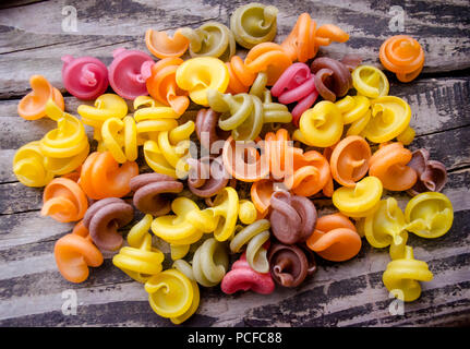 Heap of colored italian pasta on old woden desk. Bunch of raw pasta isolated on gray striped background. Stock Photo