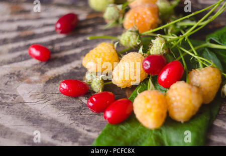 Yellow raspberry and cornel fruits with leafs on old textured wooden background. Organic berries closeup. Ripe fresh white raspberry and dogwood. Stock Photo