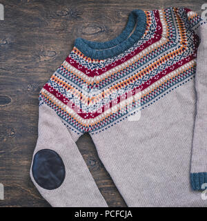 Grey, orange, bordo and beige knitted sweater on wooden background Stock Photo