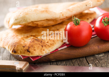 Indian naan bread and tomatoes on old wooden table. Stock Photo