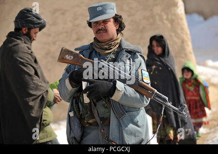 An Afghan National Police member provides security while other members distribute food and cold-weather clothing in Molla Owrang village, Nawbahar district, Zabul province, Afghanistan, Feb. 7.  The items assist the villagers through the harsh winter months. Stock Photo