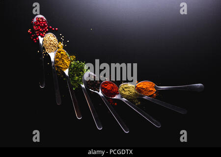 Composition of small spoons full of spices and condiments for cooking on a  black background Stock Photo - Alamy