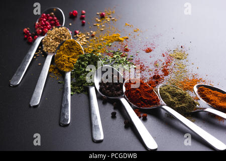 Composition of small spoons full of spices and condiments for cooking on a black background Stock Photo