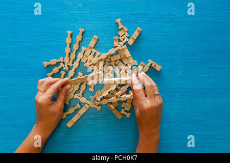 Female hands collect the details of a wooden children's designer on a blue background, a puzzle made of wooden elements. Toy for the development of mo Stock Photo