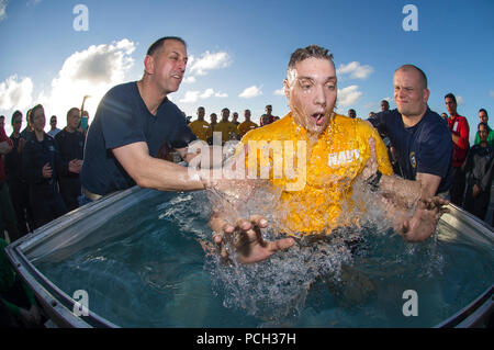 WATERS NEAR HAWAII (Aug. 2, 2015) Lt. Cole Yoos, the command religious ministries department divisional officer aboard the Nimitz-class aircraft carrier USS George Washington (CVN 73), and Lt. Brian Kirschenbaum, a Carrier Air Wing (CVW) 5 chaplain, baptize Aviation Structural Mechanic (Safety Equipment) 2nd Class Ryan Norton, from Minto, N.D., in the baptismal pool on the ship's flight deck during a baptism-at-sea. George Washington and its embarked air wing, CVW-5, are en route to conduct a hull-swap with the Nimitz-class aircraft carrier USS Ronald Reagan (CVN 76) after serving seven years  Stock Photo