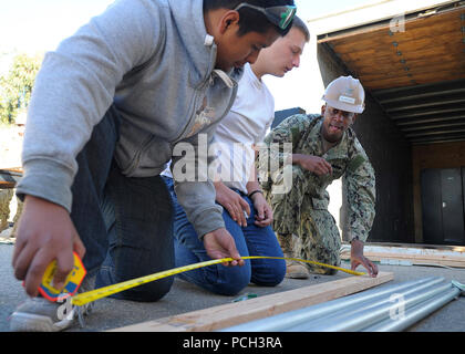 OXNARD, Calif. (Feb. 23, 2013) Engineering Aid 1st Class Willie Blanding, assigned to Naval Mobile Construction Battalion (NMCB) 3, shows Oxnard High School Junior Reserve Officer Training Corps (JROTC) students how to correctly measure wood. Volunteers from NMCB 3's First Class Petty Officer Association visited to the school to help mentor JROTC students and build shelving units for a large metal storage container. NMCB 3 provides combatant commanders and Navy component commanders with combat-ready warfighters capable of general engineering, construction and limited combat engineering across  Stock Photo