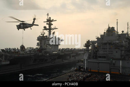 ARABIAN GULF (Feb. 15, 2018) An MH-60S Sea Hawk helicopter assigned to the Indians of Helicopter Sea Combat Squadron (HSC) 6 transports cargo from the dry cargo and ammunition ship USNS Alan Shepard (T-AKE 3) to the aircraft carrier USS Theodore Roosevelt (CVN 71) during a replenishment-at-sea. Theodore Roosevelt and its carrier strike group are deployed to the U.S. 5th Fleet area of operations in support of maritime security operations to reassure allies and partners and preserve the freedom of navigation and the free flow of commerce in the region. Stock Photo