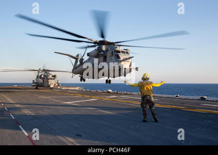 A U.S. Sailor directs a Marine Corps CH-53E Super Stallion helicopter to take off from the amphibious assault ship USS Kearsarge (LHD 3) in the Atlantic Ocean Sept. 21, 2014. The Kearsarge was underway conducting sea trials. Stock Photo