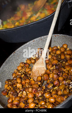 Roasting tasty crunchy chickpeas in a frying pan in a restaurant kitchen with a wooden spoon Stock Photo