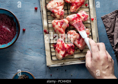 Male hand lubricates chicken wings cranberry sauce for cooking, top view. Man preparing healthy food Stock Photo