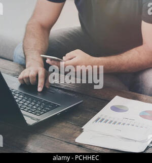 Man works laptop and smartphone on the sofa at home. Work at home concept Stock Photo