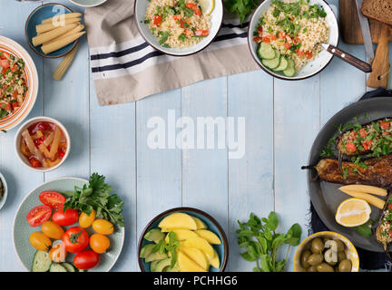 Frame from various vegetarian dishes on blue rustic wooden table. Salad with bulgur porridge and vegetables, stuffed eggplants, snacks, vegetables and Stock Photo
