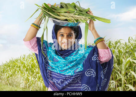 Rural woman carries corn leaves and rice on her head Stock Photo