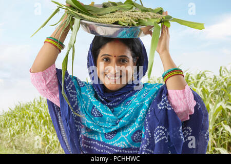 Rural woman carrying  paddy and corn leaves in plate on head Stock Photo