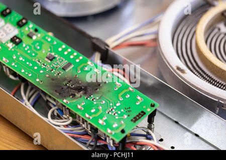 Burnt green microchip after short circuit due to water damage. Damaged overheat control panel board of cooking stove Stock Photo