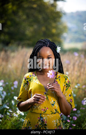 Young African woman holding a flower in a field Stock Photo