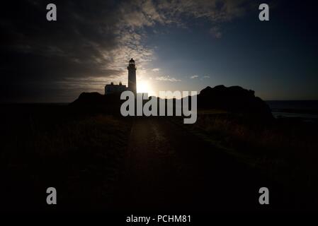 Silhouette of a lighthouse (Turnberry Lighthouse) along the Ayrshire Coast next to the Trump Turnberry Golf Course, with the sunset in the background. Stock Photo