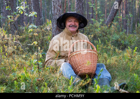 Portrait of relaxed mature man sitting in the forest with basket. Stock Photo