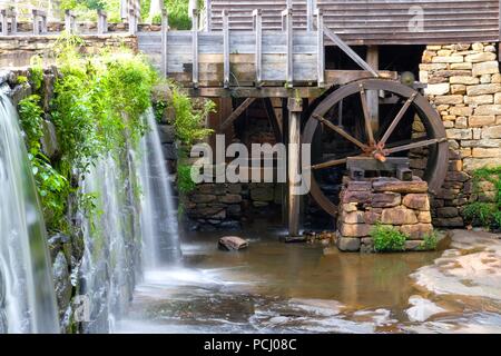 The greenery droops over the waterfall with the flume and waterwheel in view at Historic Yates Mill County Park in Raleigh North Carolina Stock Photo