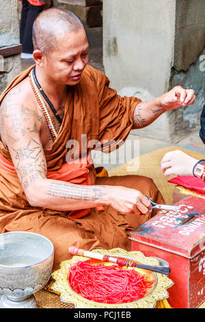 Angkor Wat, Cambodia - 11th January 2018: Monk giving blessings and tying good luck string bracelets. This is in exchange for donations. Stock Photo