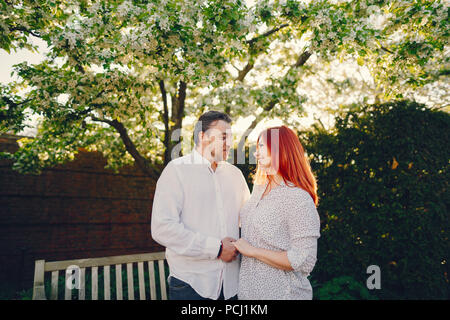 beautiful and stylish redhead woman in a white blouse standing in a sunny summer park with her handsome husband Stock Photo