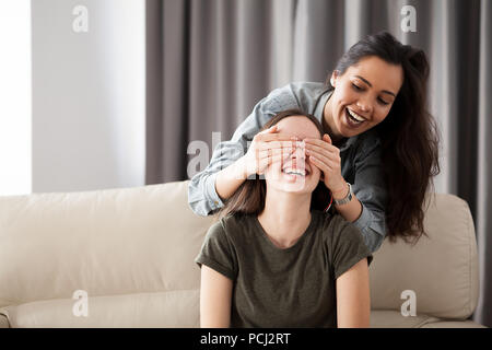 Two girlfriends are playing hide and seek on the couch in the living room Stock Photo