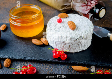 round head of blue cheese with honey, currant berries, nuts and a bottle of wine on a dark table, concept of gourmet food, Italian cheese, romantic ev Stock Photo