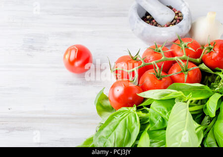ripe tomatoes, a lot of green basil and , garlic, salt and Spices in a stone mortar on white old rustic wooden background. Top view, Copy space. Stock Photo