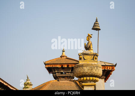 Durbar square in Bakhtapur, Nepal, with temple roofs and votive column with golden sitting figure under an umbrella. Stock Photo