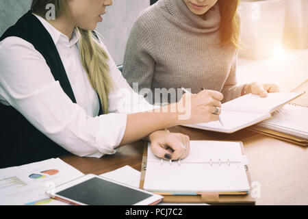 Two hard working young female entrepreneurs working together on office desk reading report with serious engrossed expressions. Stock Photo