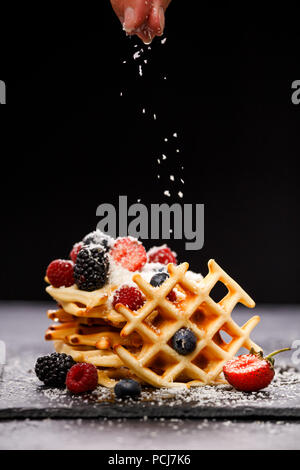 Photo of viennese wafers with raspberries, strawberries sprinkled with powdered sugar on blackboard against blank background Stock Photo