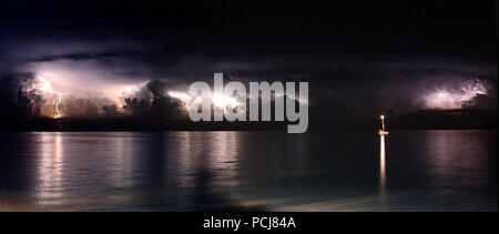 Multiple forks of lightning during a thunderstorm over the ocean. Panoramic with lone boat lit up at night Stock Photo