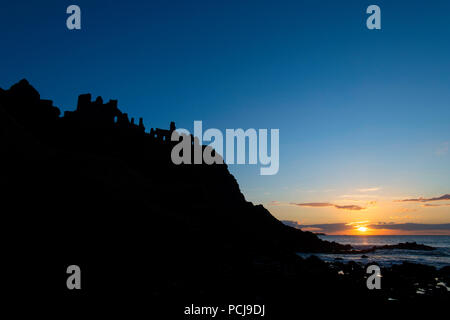Ruins of Dunluce castle silhouetted by the sunsetting on the Irish coast Stock Photo