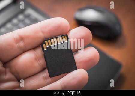 Male Hand Holding An SD Card With Laptop Computer And Mouse In Background, Extent Disk Space Concept Stock Photo